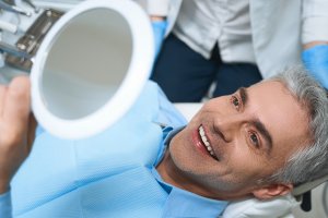 man in dental chair smile into hand mirror