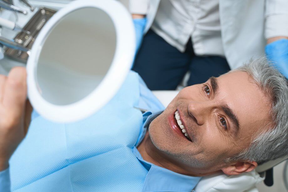 man in dental chair smile into hand mirror